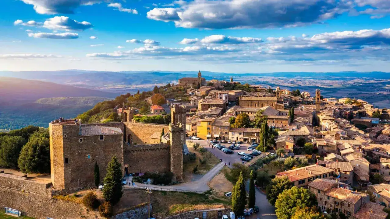 Un borgo medievale arroccato su una collina, con un castello imponente e case in pietra. Un gioiello tra i borghi da visitare nel nord Italia, sotto un cielo azzurro con nuvole bianche.