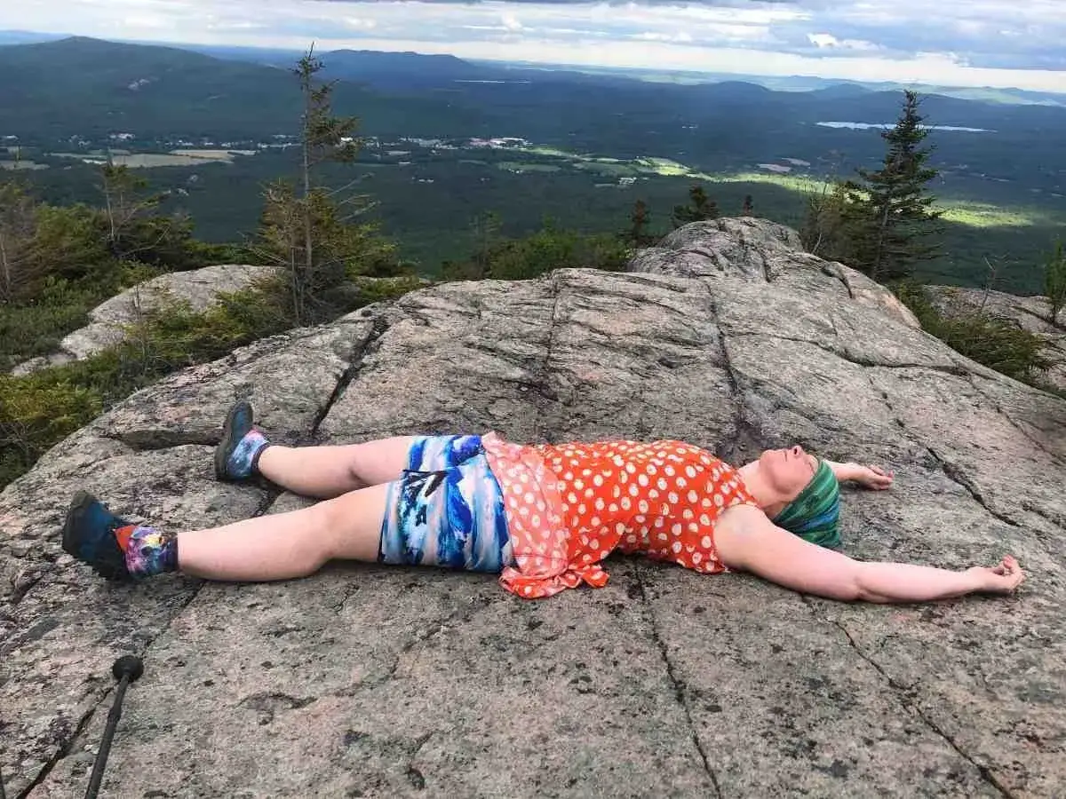 Donna si gode il panorama dall'alto, sdraiata su una roccia con un gita outfit montagna estate colorato.