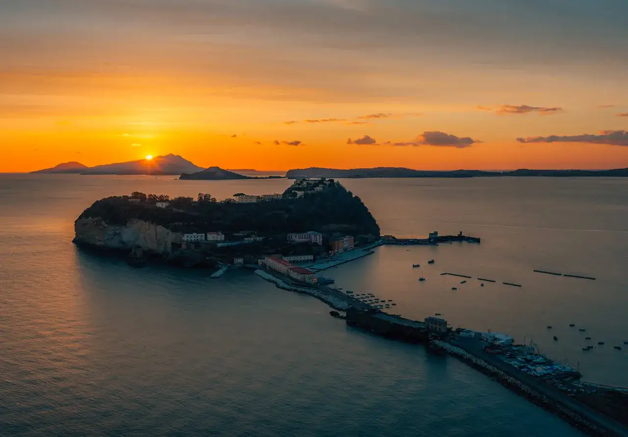 Tramonto infuocato sul golfo di Napoli, con una suggestiva isoletta che si staglia sul mare calmo e le sagome delle isole all'orizzonte.