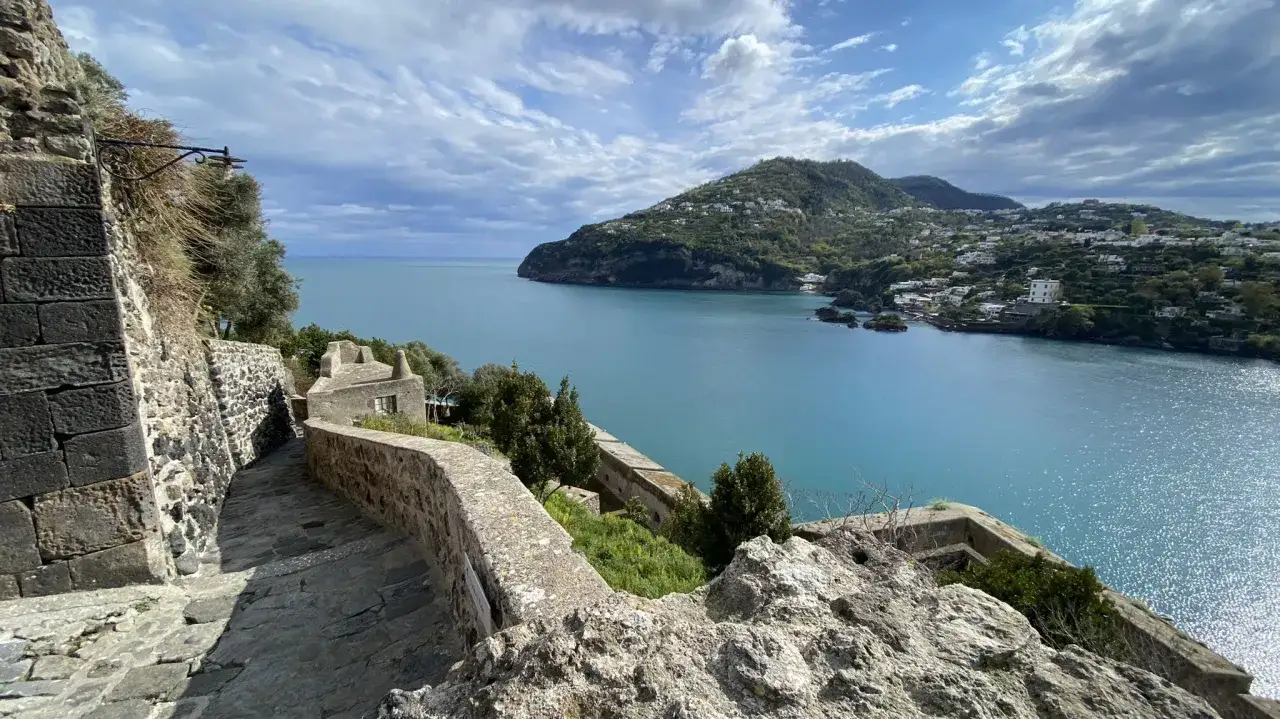 Sentiero in pietra con vista sul mare azzurro e colline verdi. Perfetto per scoprire cosa vedere a Ischia in un giorno.