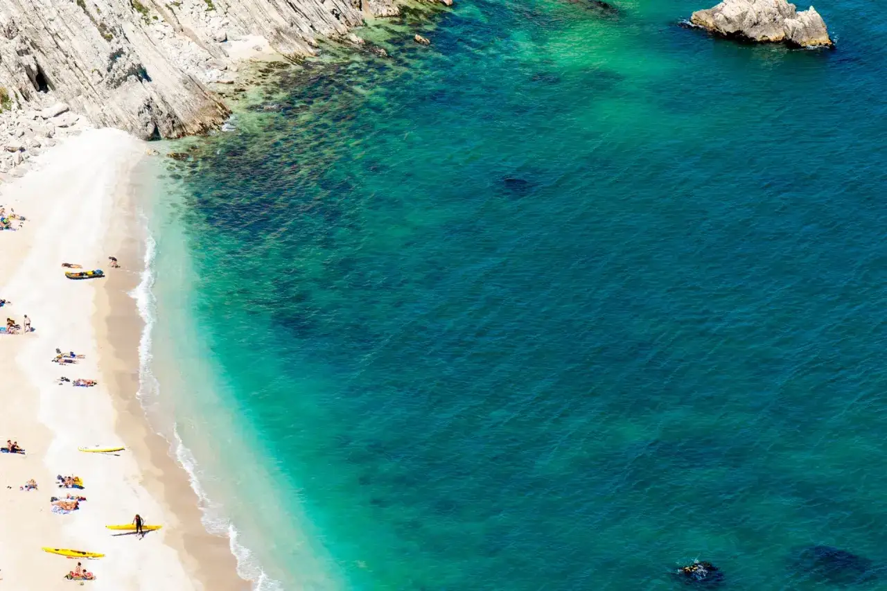 Spiaggia di sabbia bianca baciata da acque turchesi, ideale per scoprire le migliori spiagge del nord Italia. Persone rilassate e kayak gialli.