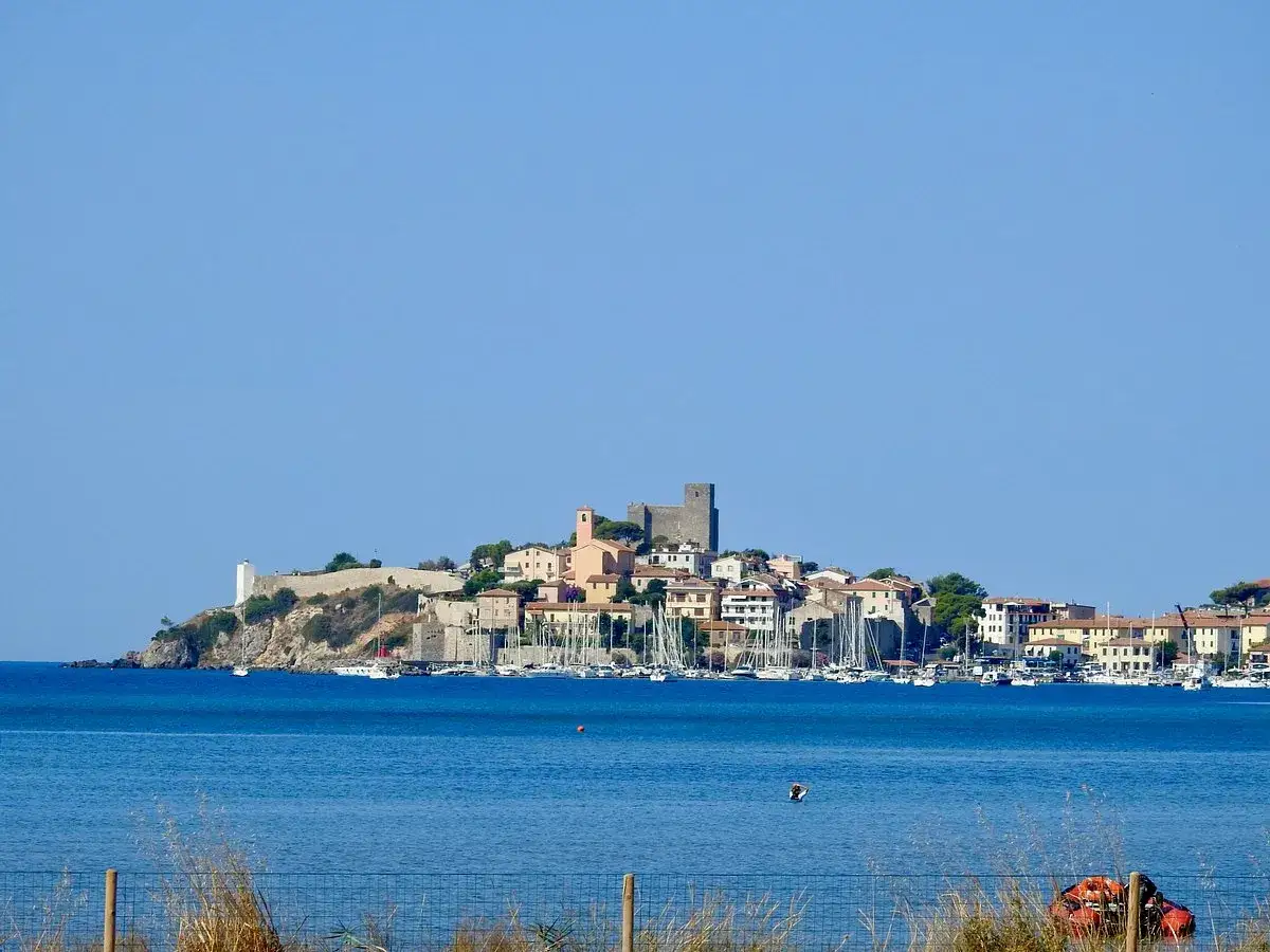 Il Talamone centro storico si affaccia sul mare blu, con un castello e case arroccate sulla collina. Barche a vela nel porto.