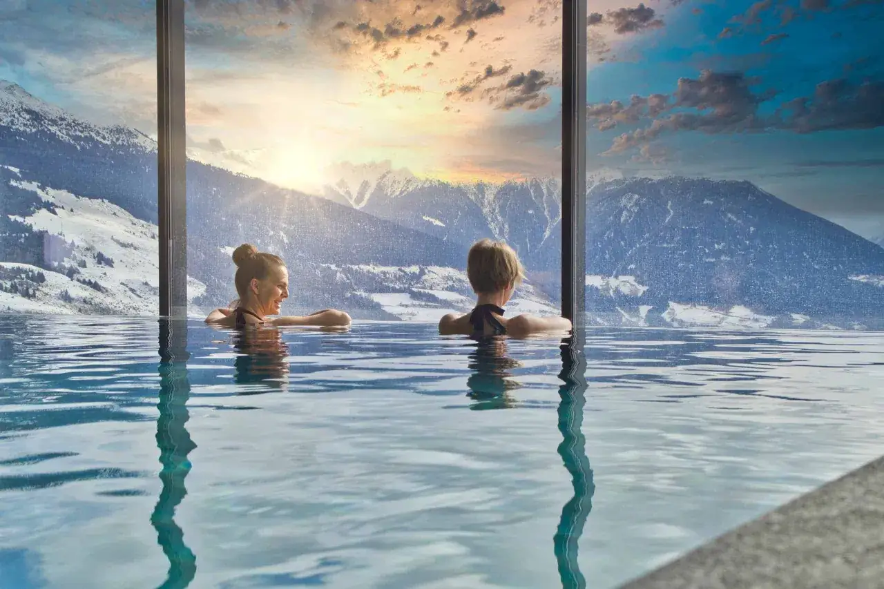 Due persone rilassate in una piscina a sfioro con vista sulle montagne innevate, un'esperienza unica nelle terme in Trentino Alto Adige.