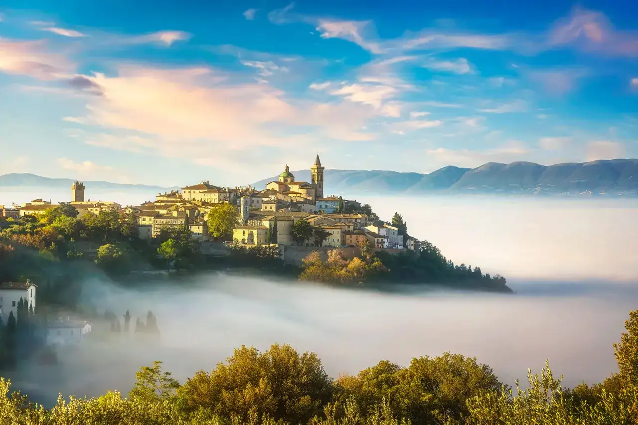 Borghi vicino Foligno avvolti dalla nebbia al tramonto, con montagne sullo sfondo e cielo colorato.