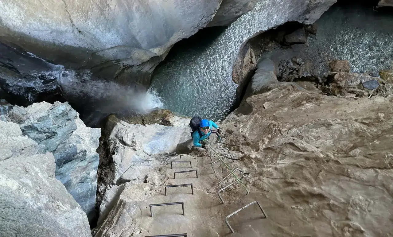 Persona su una scala metallica in una gola, affronta le ferrate Val di Susa con una cascata e acqua cristallina.