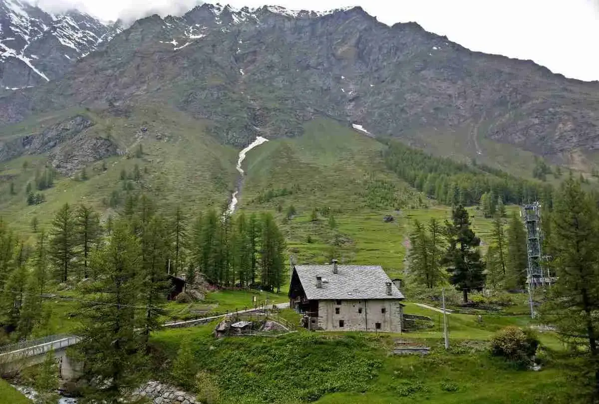 Un casolare in pietra nel Val di Rhemes, circondato da verdi pendii e imponenti montagne innevate.