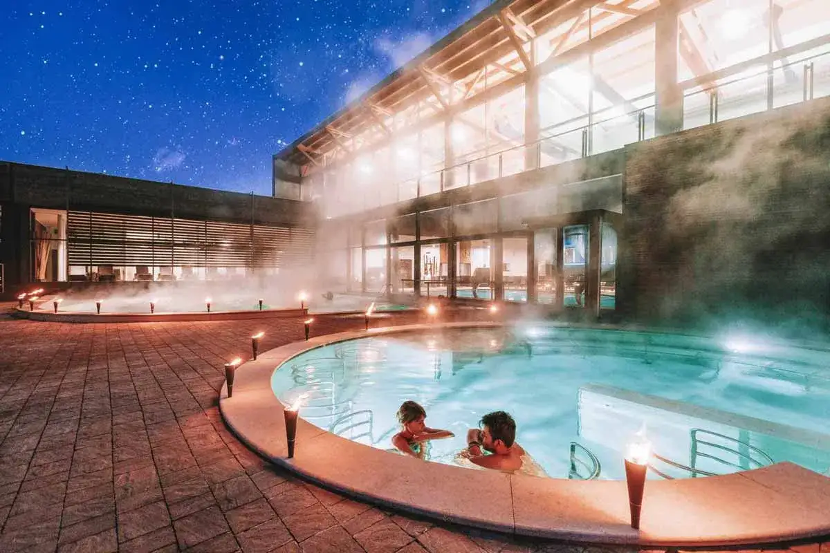 Coppia rilassata in una piscina termale all'aperto, con vapore che sale verso il cielo stellato. Un'oasi di benessere, perfette terme vicino Milano.