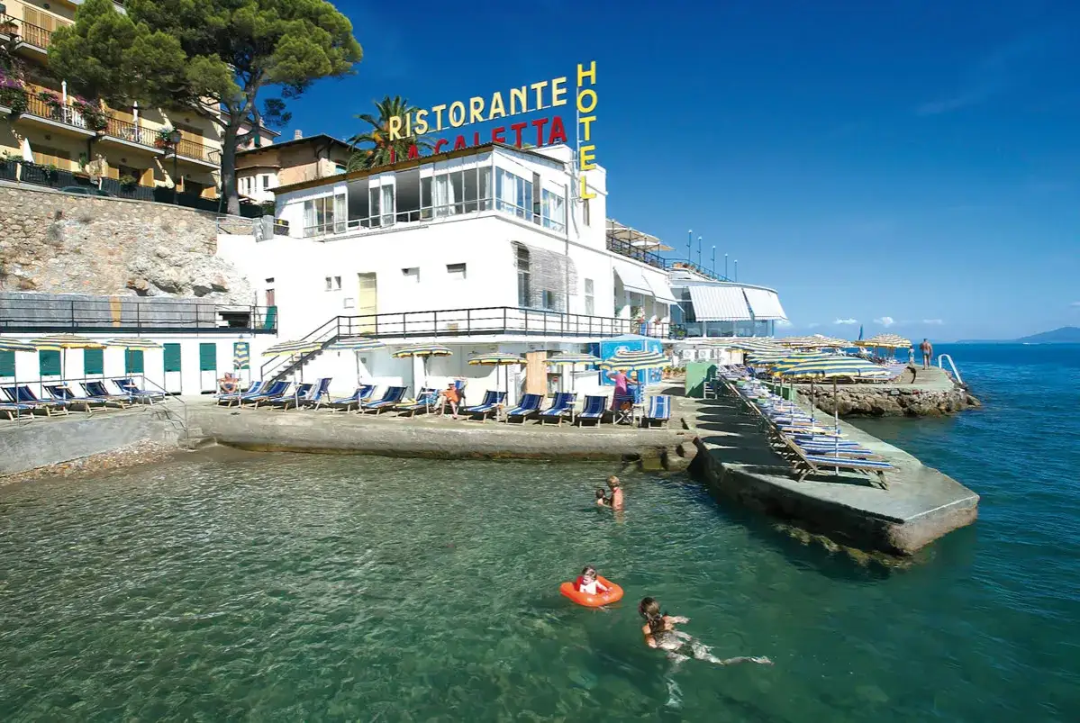 Calette a Porto Santo Stefano con gente che nuota e si rilassa sotto gli ombrelloni.