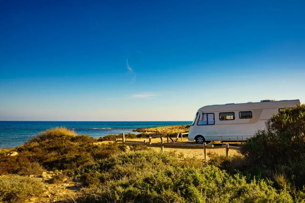 Un camper bianco sosta su un sentiero sterrato con vista sul mare blu intenso. Un'avventura indimenticabile in Isola d'Elba in camper.