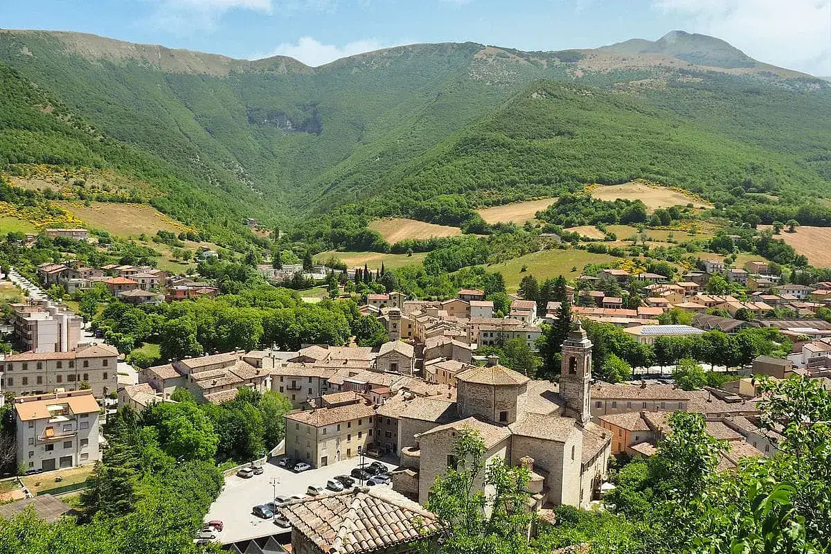 Un incantevole panorama di borghi da visitare nelle Marche, con case in pietra e tetti in cotto, incastonati tra verdi colline e montagne.