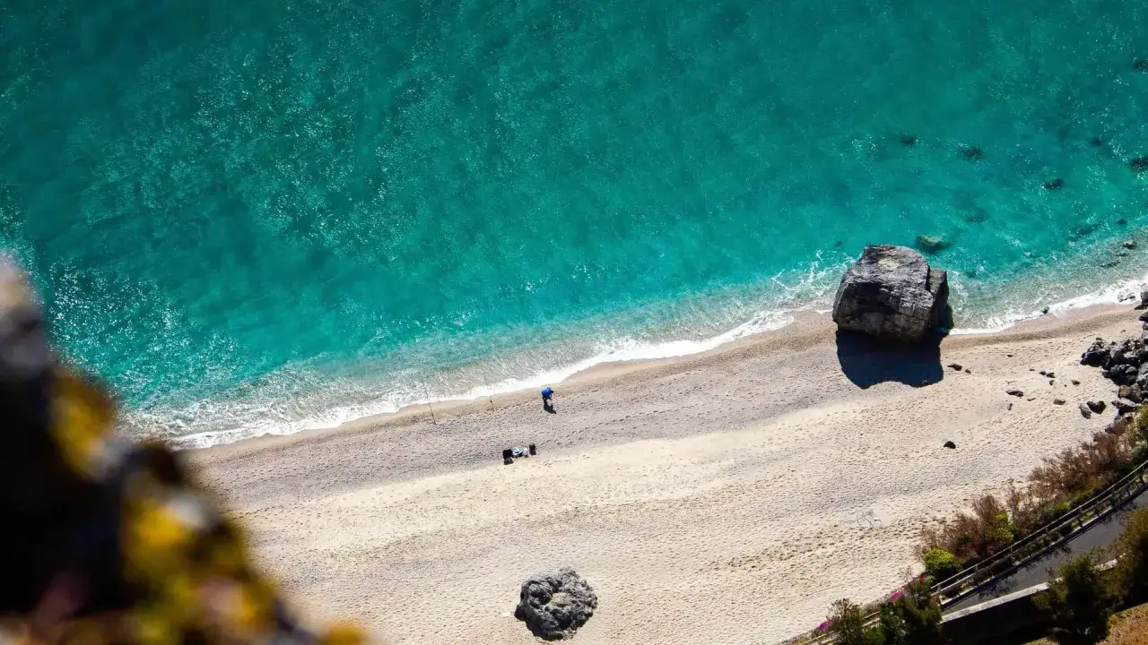 Spiaggia dorata e mare cristallino sulla riviera ligure di ponente. Un pescatore solitario e rocce imponenti.