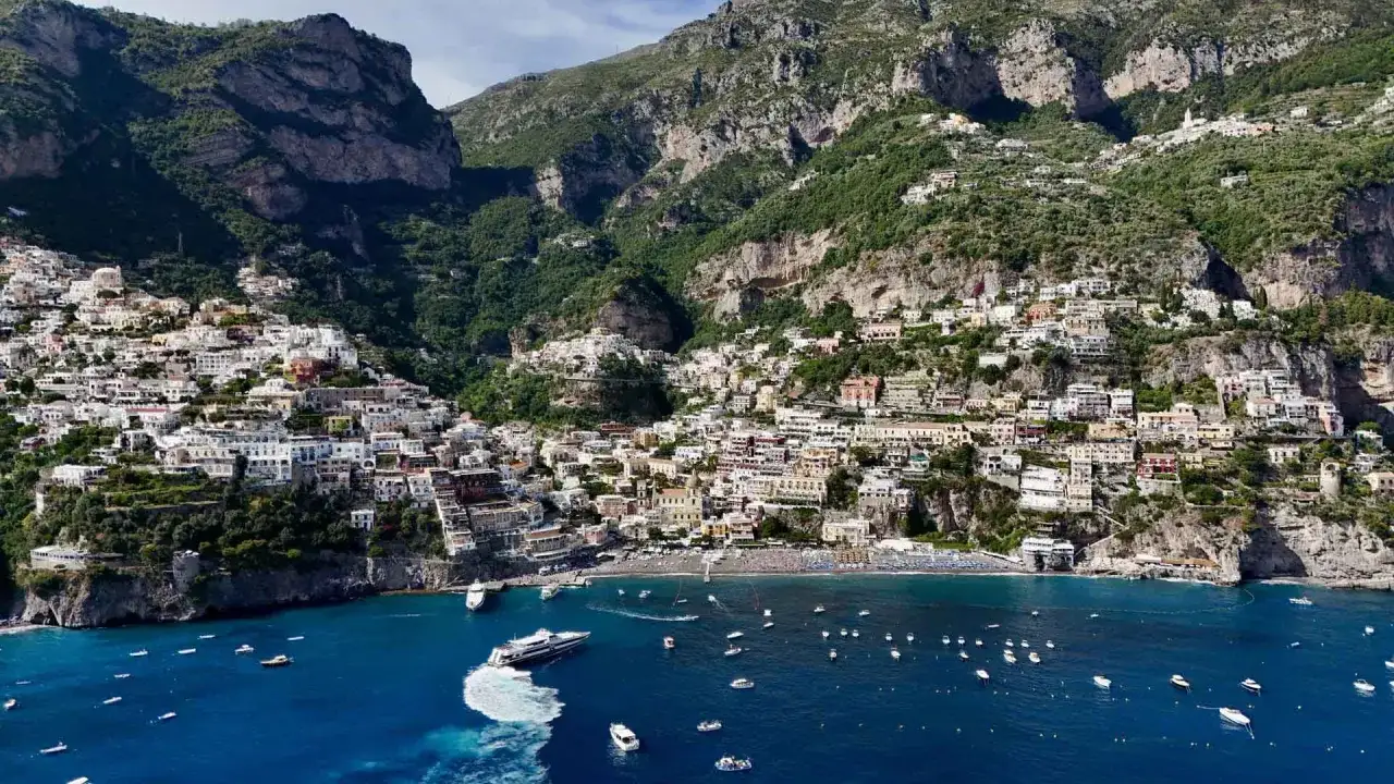 I paesi della Costiera Amalfitana aggrappati alla scogliera, con case colorate che scendono verso il mare blu e barche che navigano.