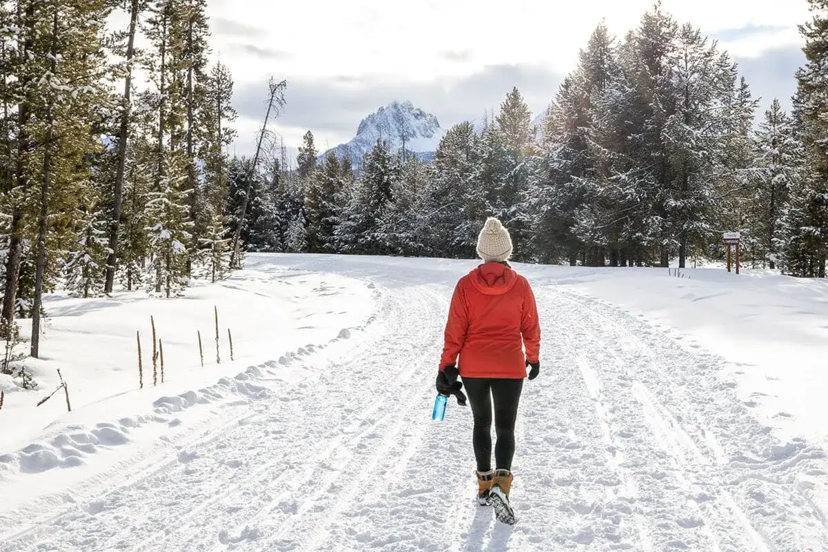 Donna con cappello e giacca arancione cammina su un sentiero innevato, un esempio di come vestirsi per andare sulla neve.