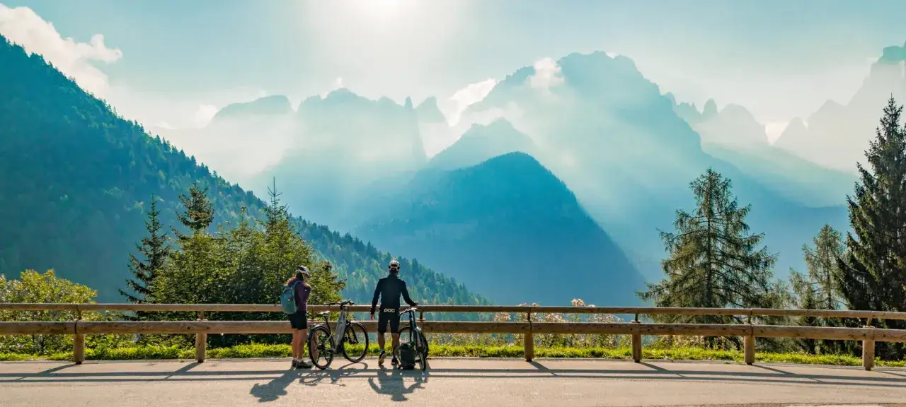 Coppia di ciclisti ammira i maestosi panorami delle Dolomiti, pronti a esplorare i loro percorsi bici.