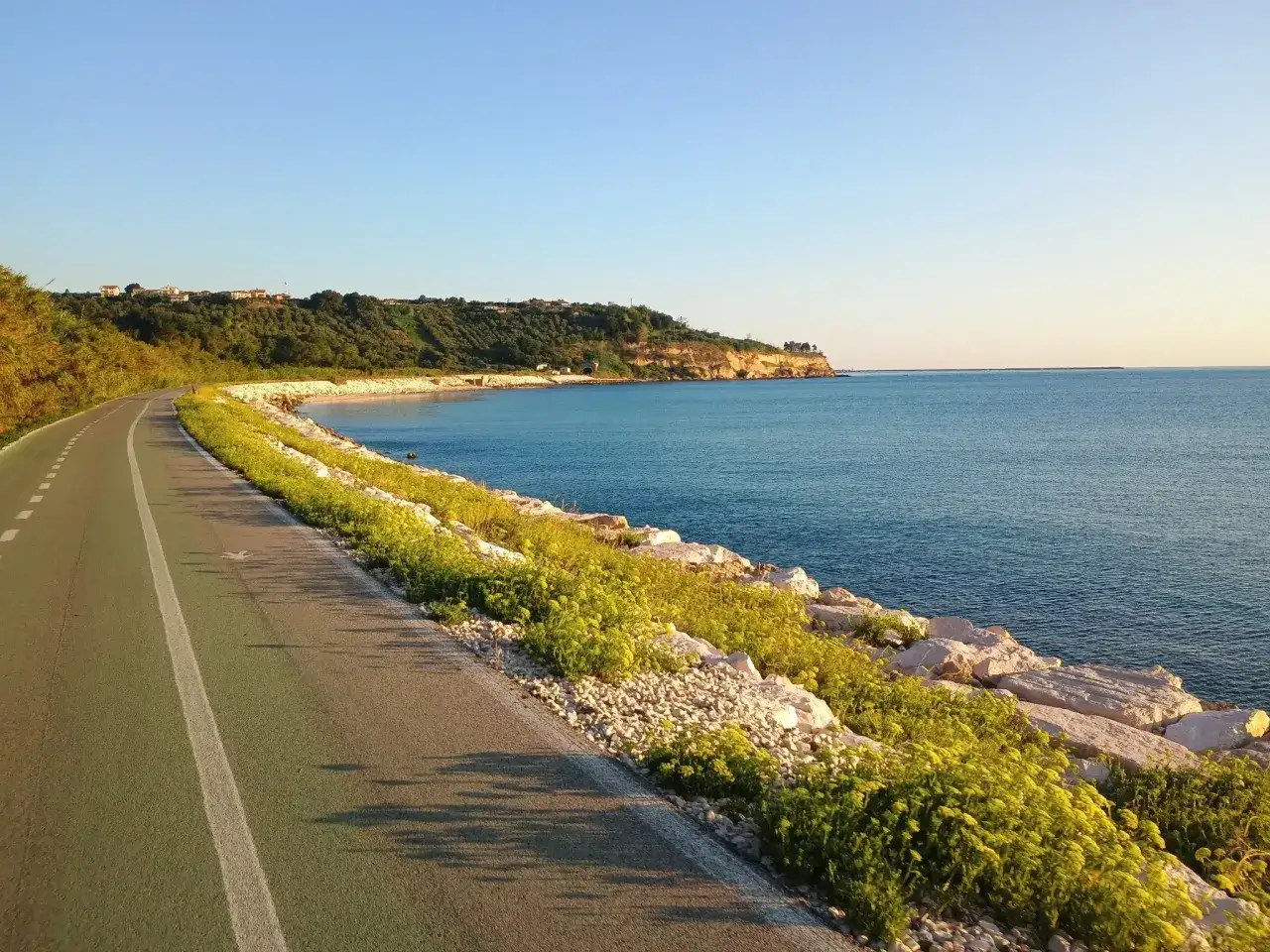 Ciclovia Adriatica Abruzzo: una pista ciclabile costiera con vista sul mare blu, scogliere rocciose e vegetazione verdeggiante.