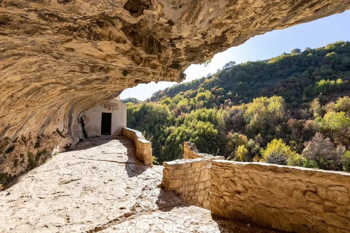 Un piccolo eremo incastonato nella roccia, con un sentiero dello spirito che conduce a un panorama boscoso.
