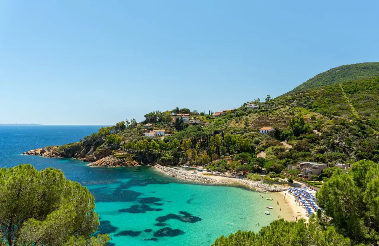 Baia con acque cristalline e spiaggia attrezzata, incastonata tra colline verdi e case bianche. Un angolo di paradiso per scoprire località mare toscana economiche.