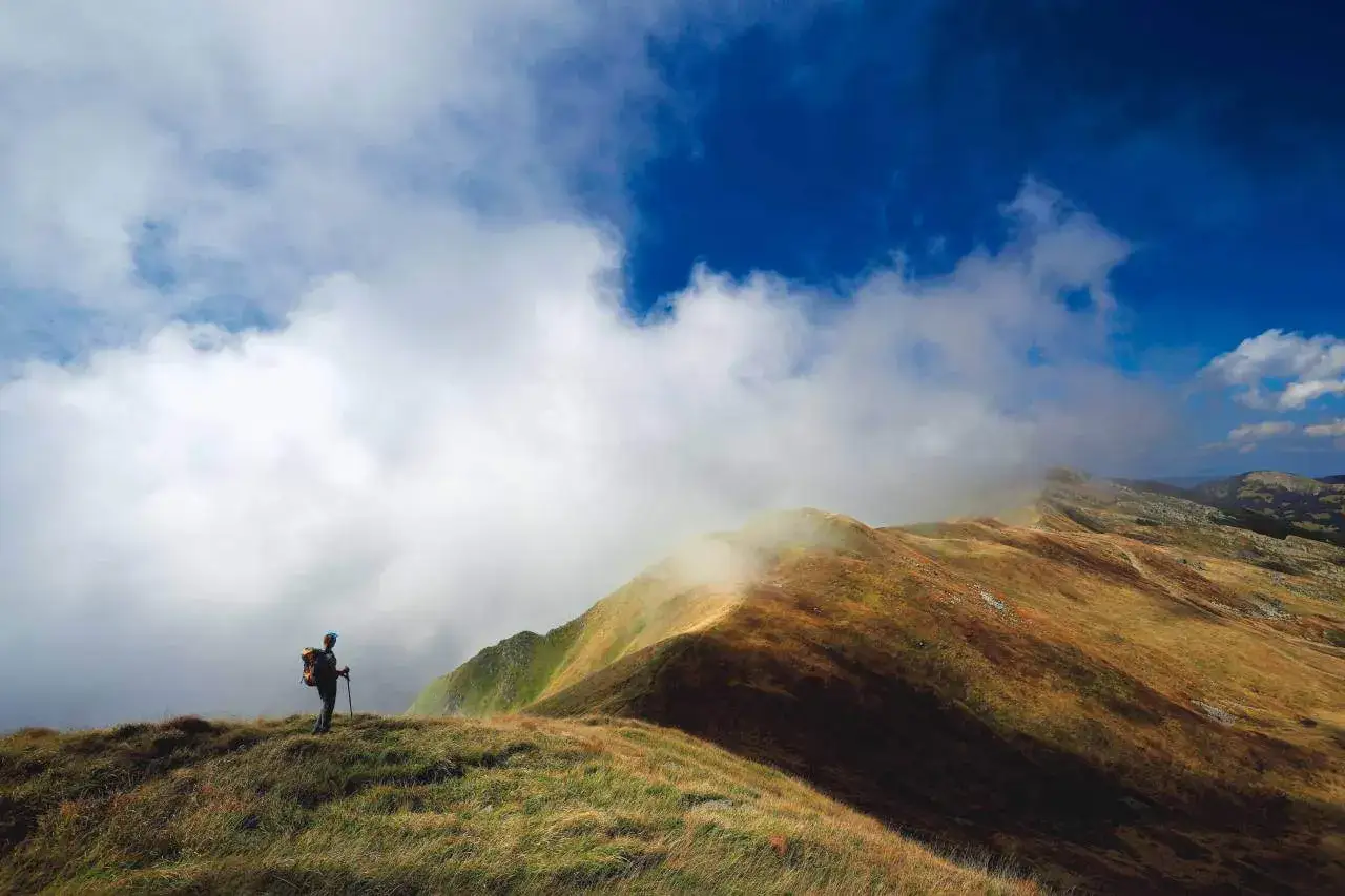 Escursionista solitario su un crinale erboso, con nuvole che avvolgono le cime dei sentieri dell'Appennino Tosco Emiliano.