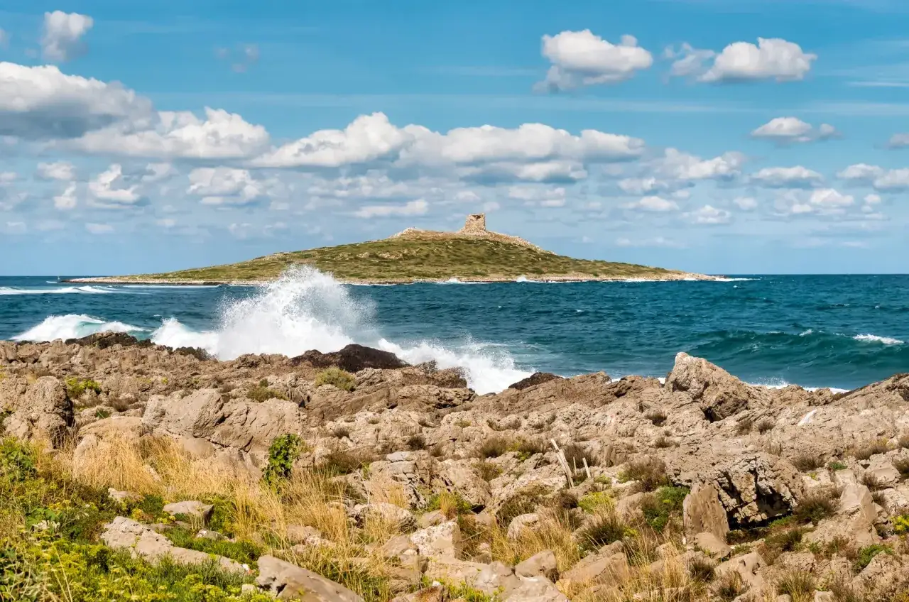 Onde si infrangono su rocce scogliere, con un'isola e una torre in lontananza. Un paesaggio marino suggestivo, tra le isole vicino Palermo.