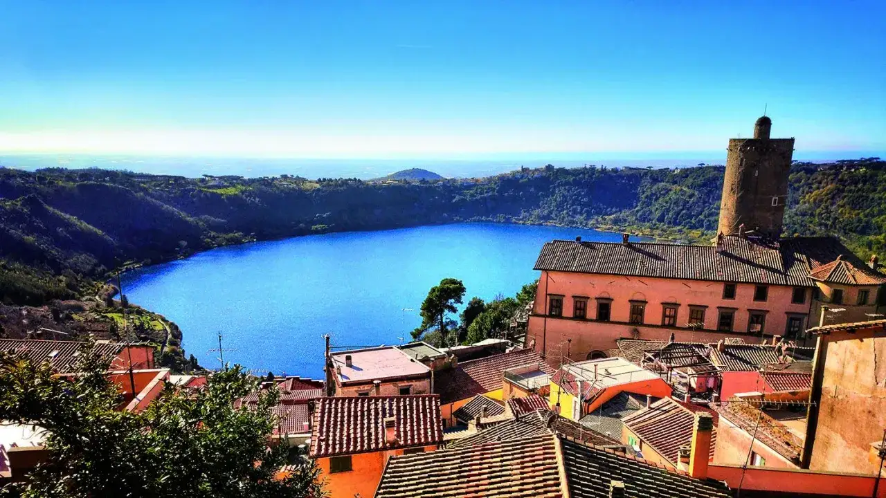 Vista di un lago blu intenso con un borgo colorato e una torre medievale. Perfetta gita fuori porta Roma inverno.