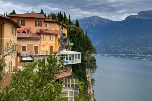 Case colorate aggrappate alla roccia a Tremosine sul Garda, con il lago e le montagne sullo sfondo.