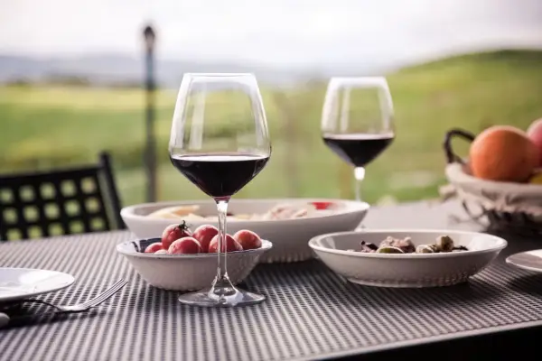 Un bicchiere di vino rosso e stuzzichini su un tavolo all'aperto, con un paesaggio collinare sullo sfondo, perfetto per un percorso enogastronomico toscana.
