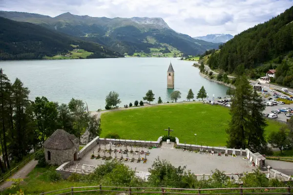 Un antico campanile nel lago, circondato da montagne verdi e un cimitero.