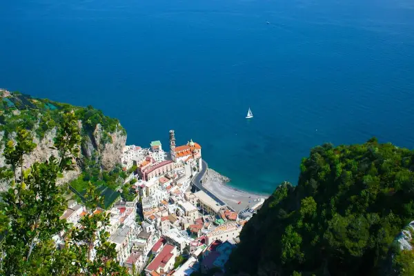 Vista dall'alto di Amalfi, con il mare blu intenso e una barca a vela. Il percorso da Amalfi a Ravello offre panorami mozzafiato.