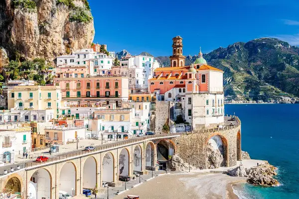 Un incantevole borgo da visitare in Campania, con case colorate aggrappate alla roccia, un ponte ad archi e il mare blu.