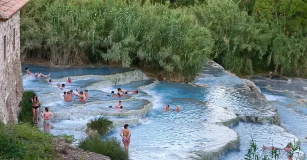 Persone si rilassano nelle cascate naturali delle terme famose in Italia, circondate da vegetazione lussureggiante.
