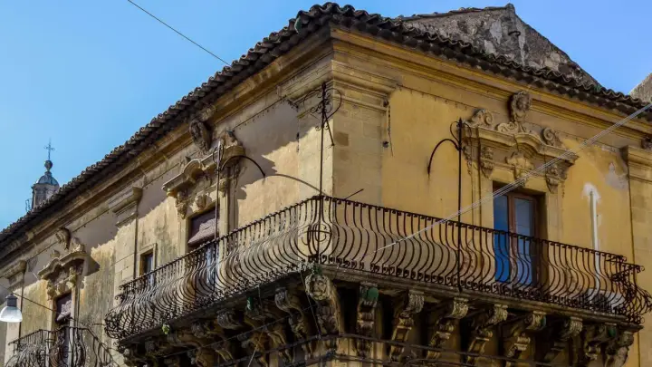 Angolo di un palazzo barocco a Militello in Val di Catania, con balcone in ferro battuto e decorazioni in pietra.