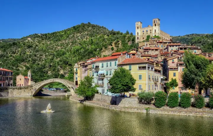 Borghi entroterra ligure levante: un ponte antico attraversa un fiume, case colorate si affacciano sull'acqua, un castello domina la collina verde.