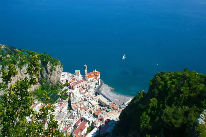 Vista dall'alto di Amalfi, con il mare blu intenso e una barca a vela. Il percorso da Amalfi a Ravello offre panorami mozzafiato.