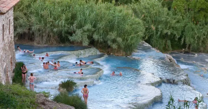 Persone si rilassano nelle cascate naturali delle terme famose in Italia, circondate da vegetazione lussureggiante.